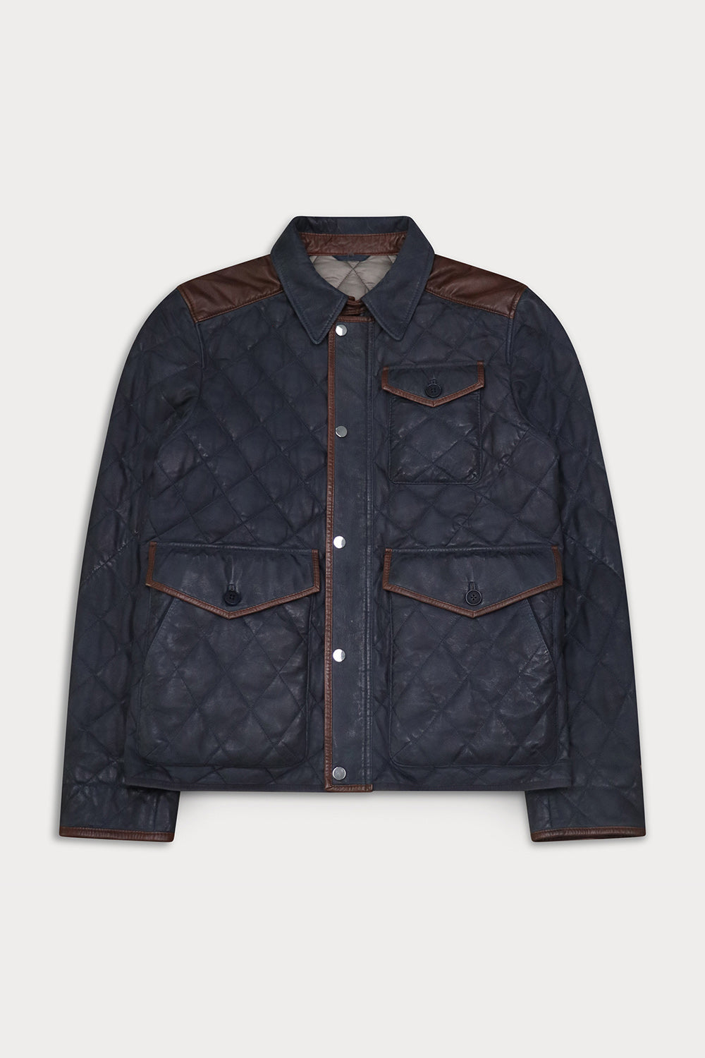 A dark navy blue quilted jacket with brown leather shoulder panels and trim, featuring a button-up front and flap pockets.