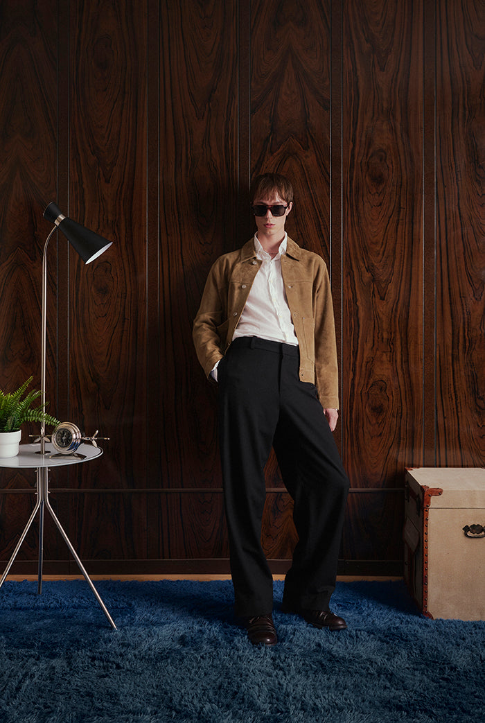 A model stands in a stylish room with dark wood paneling, wearing a brown suede jacket, Mateo from Sly&Co.